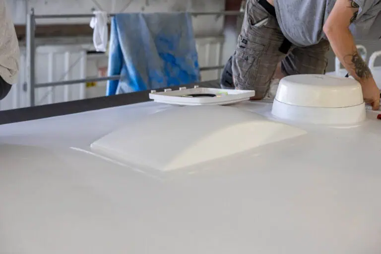 Technician working on the roof of an RV during a roof installation process, with a newly coated white roof surface, roof vent, and skylight visible in the foreground.